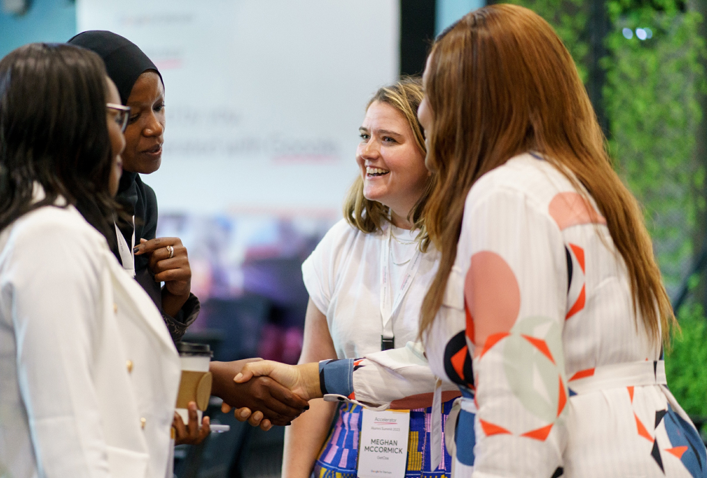 Four standing women discussing and smiling.