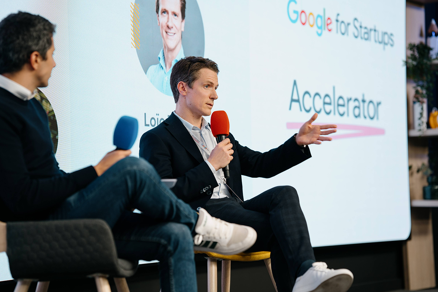 Two individuals on stage, holding microphones and speaking at the event.