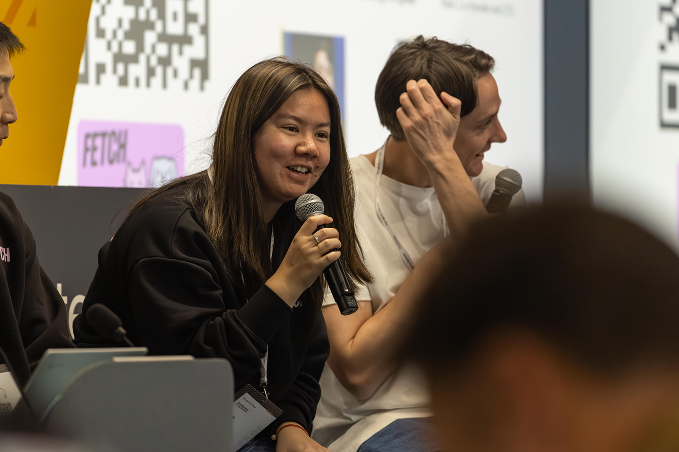 One of the event hosts, holding a mic, is speaking to the audience.