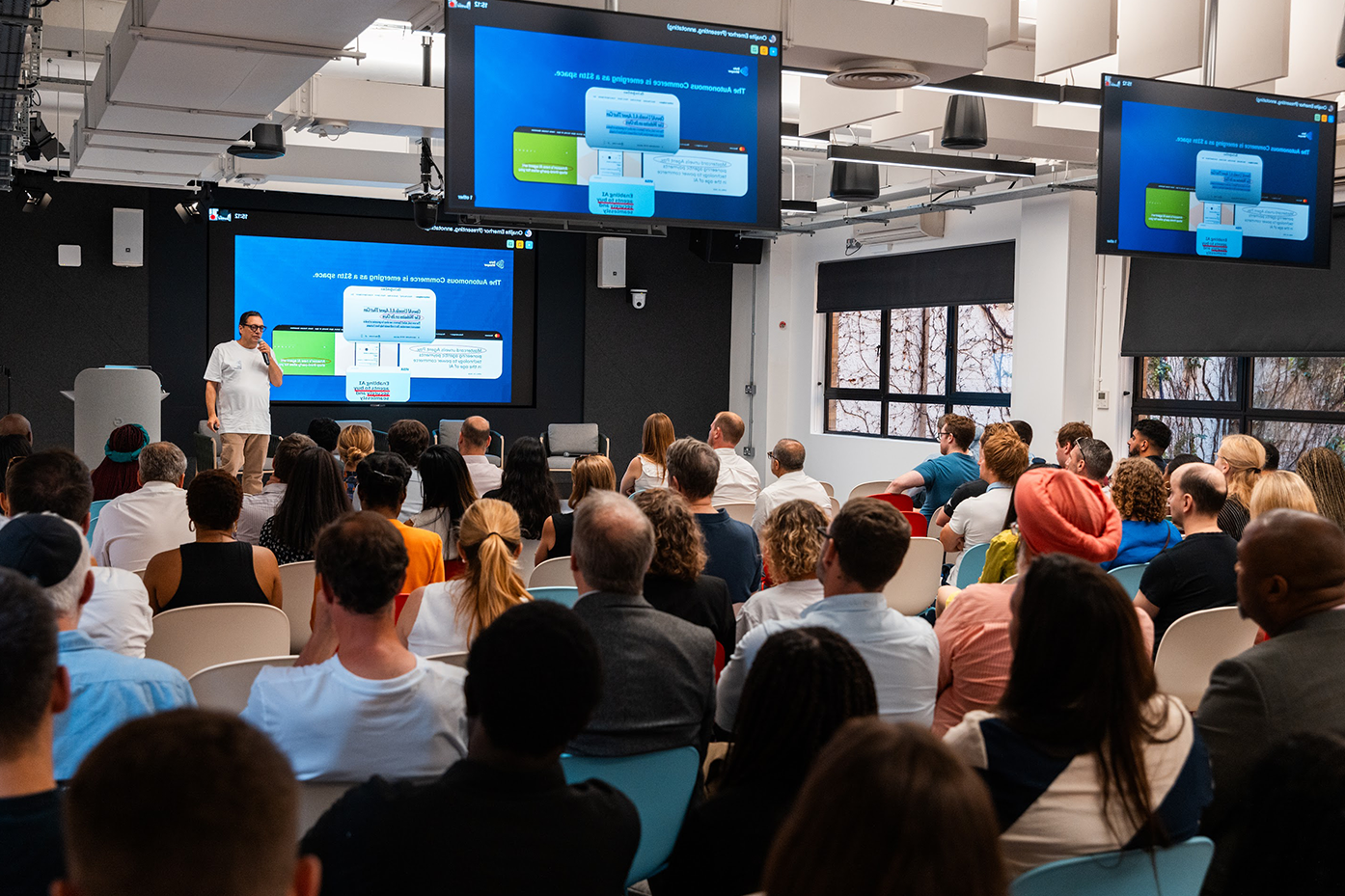The host stands before a crowded event hall.