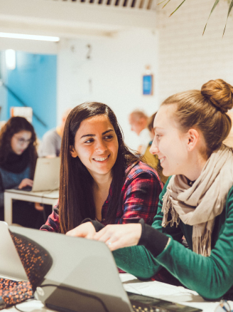 Two casual girls sitting by table in front of laptop