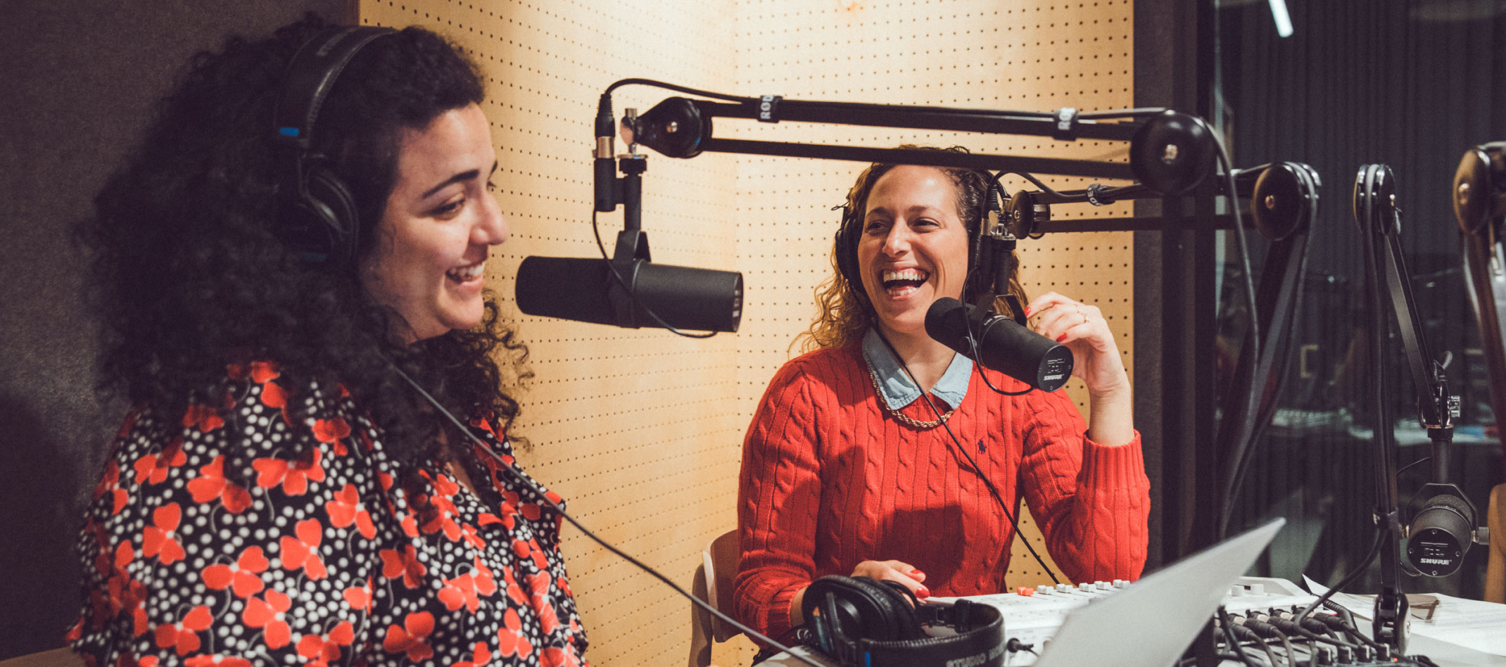 Two multiracial women are sitting at recording studio while recording.