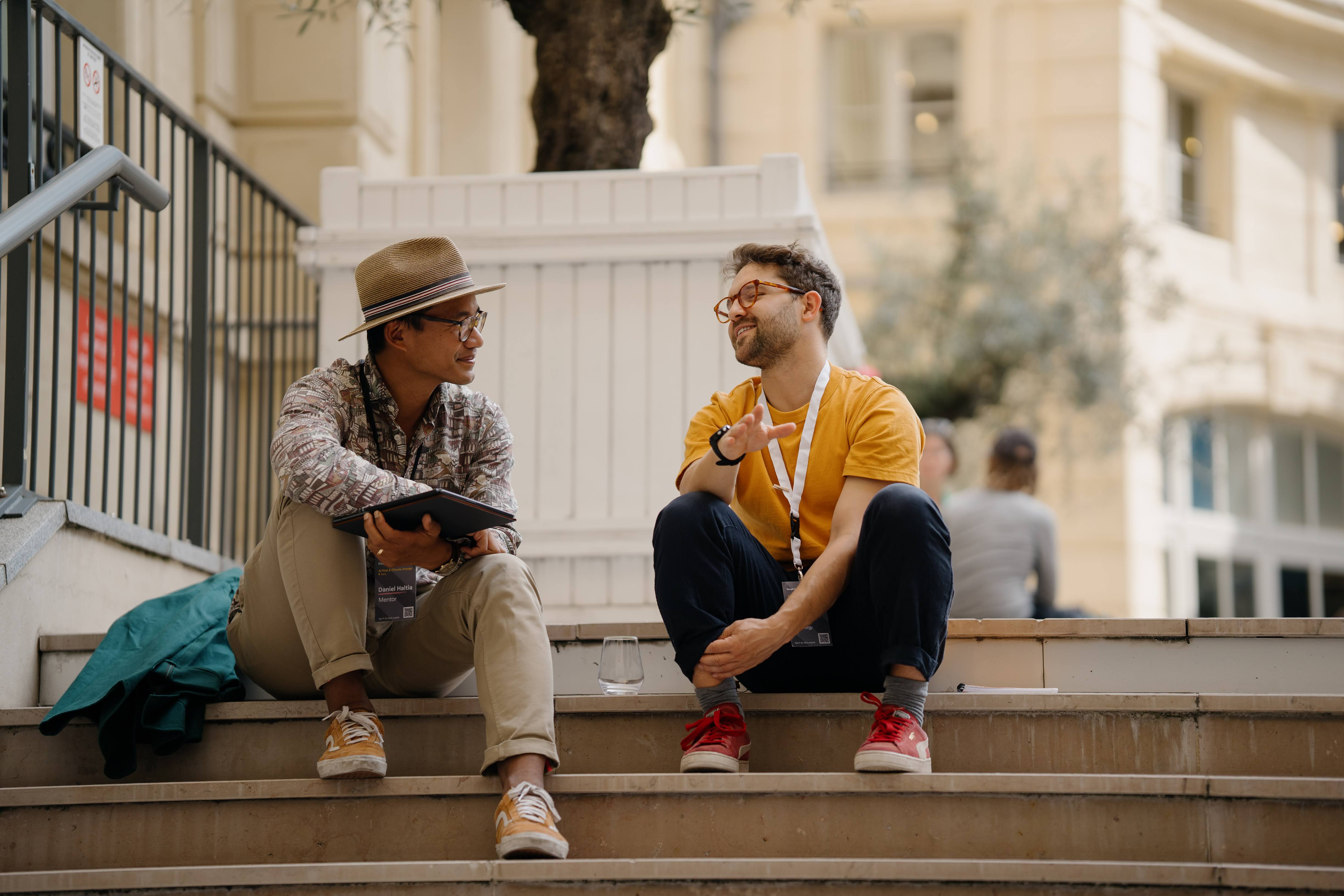 Two people are sitting on the stairs while one of them is holding a tablet.