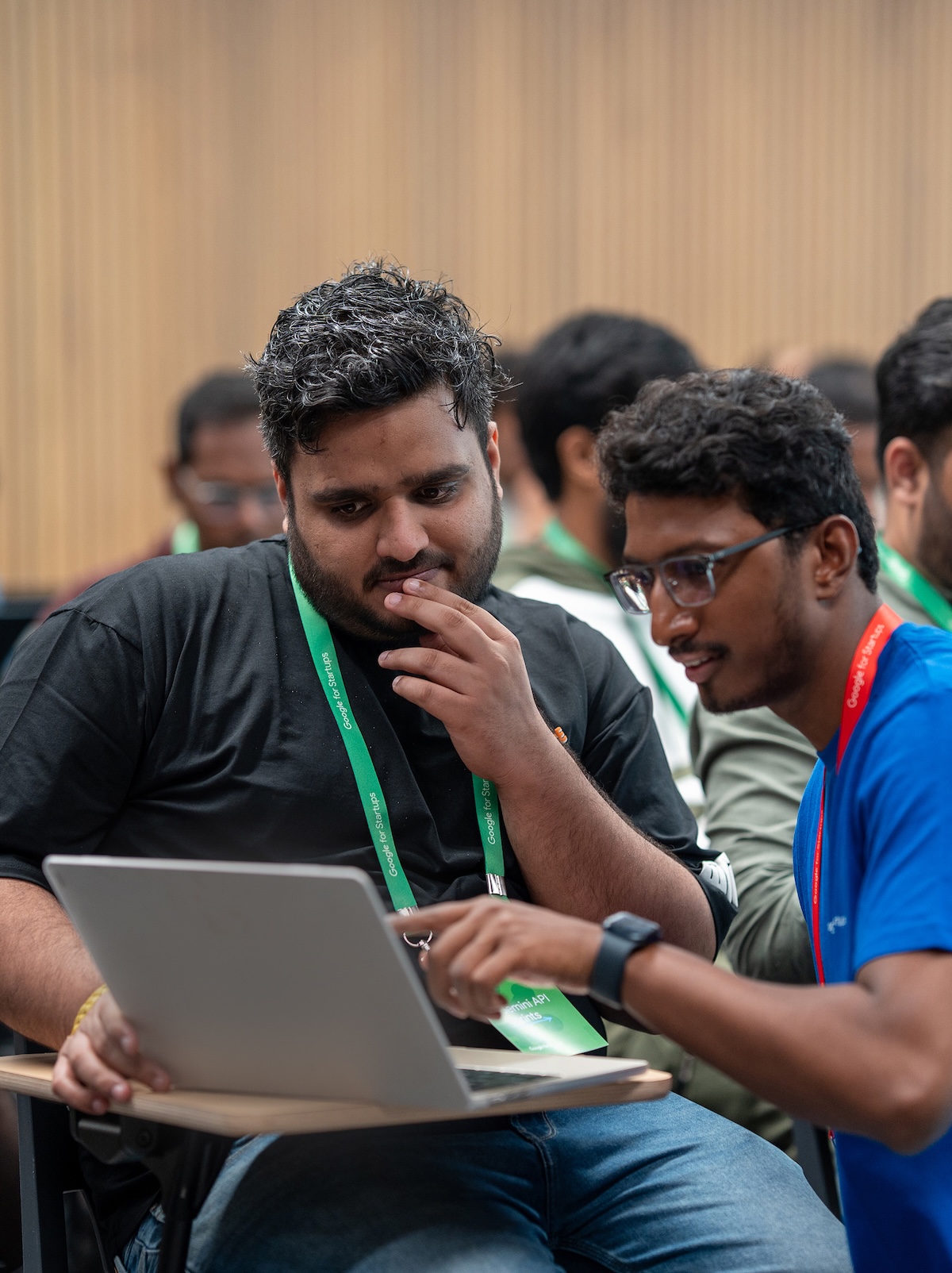 A man in blue shirt showing something one a laptop to another man.
