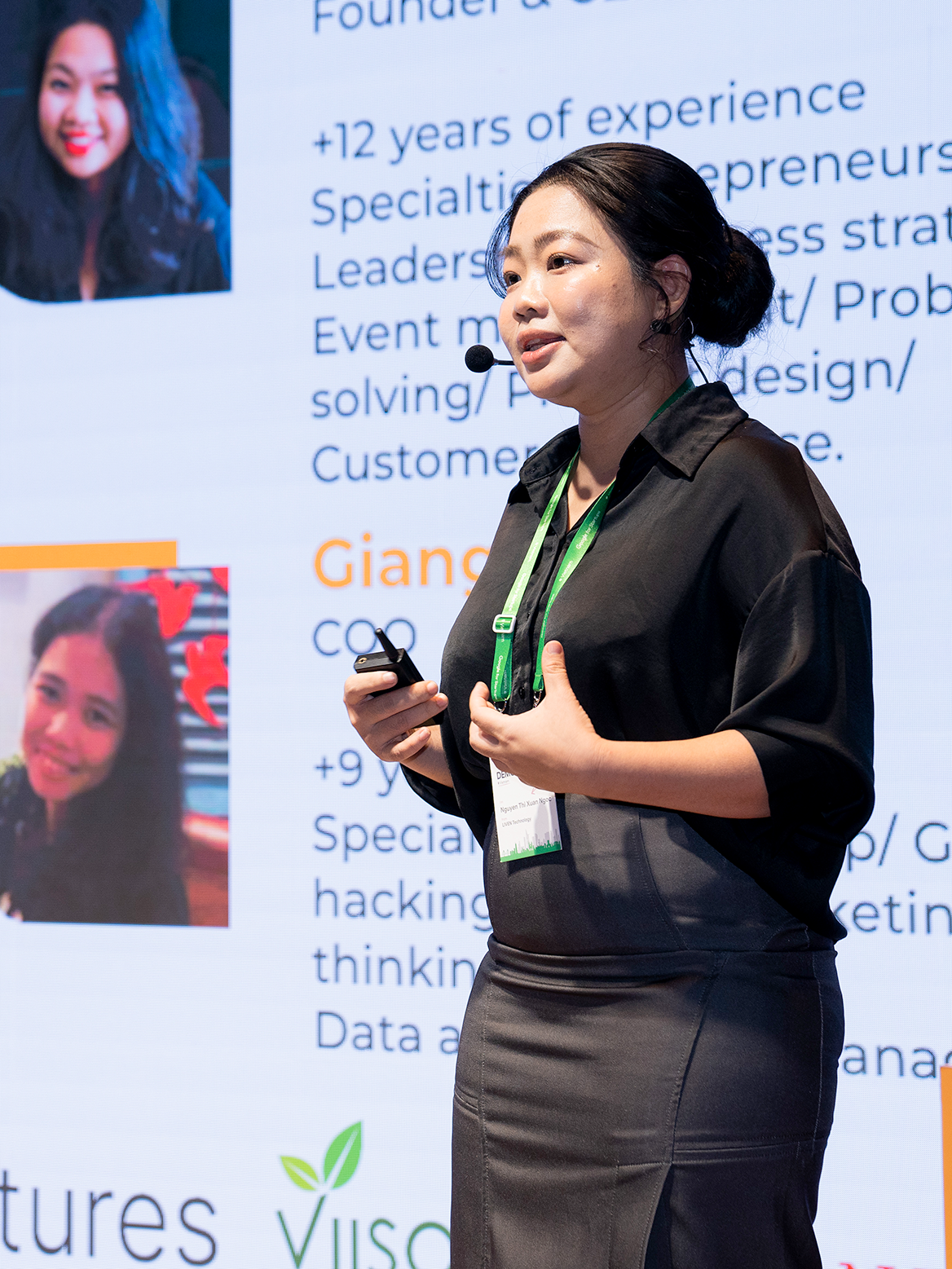 A woman in a black dress is speaking while looking infront.