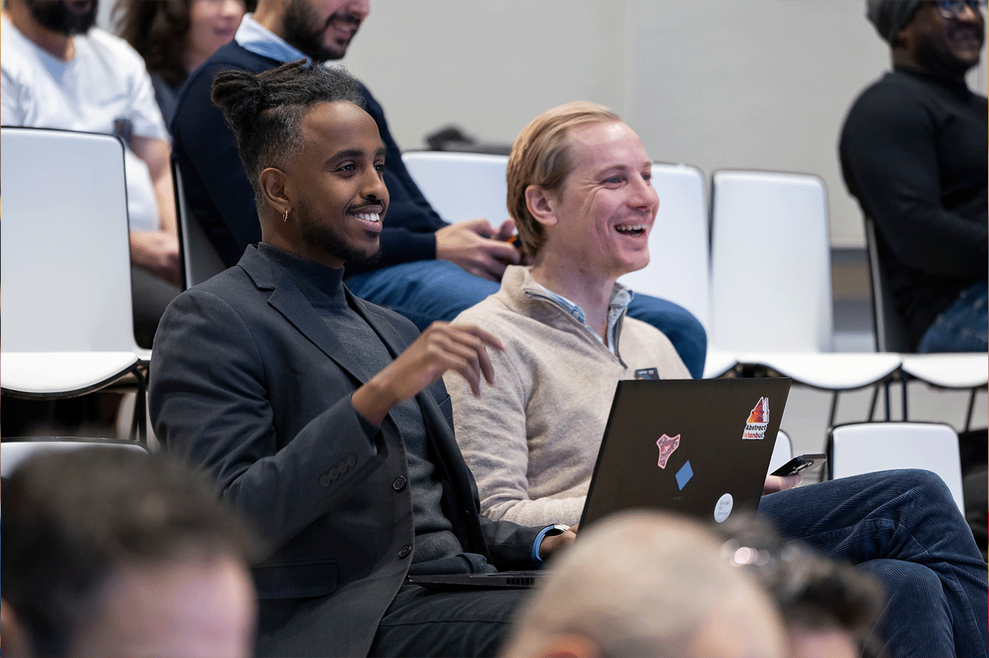 One person in the audience, with a laptop in front, is talking and smiling at the host.