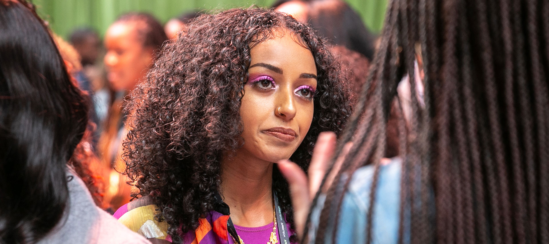 A woman with curly hair is listening to other woman in crowd