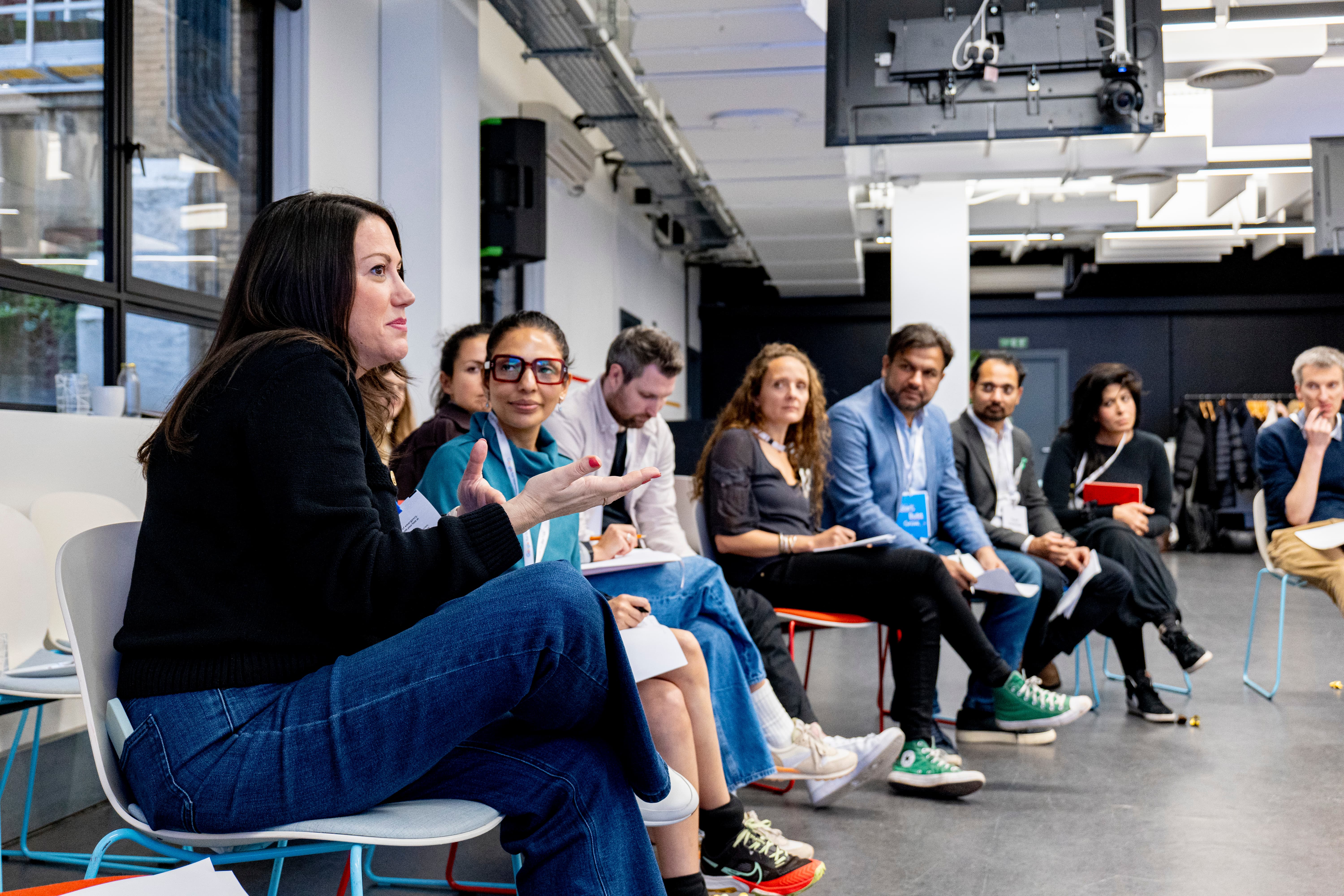 1 人の女性が説明し、他の人たちがそれを聞いている。