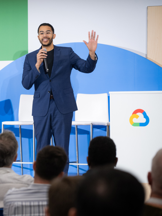 A person speaking into a microphone next to a podium with a cloud logo.