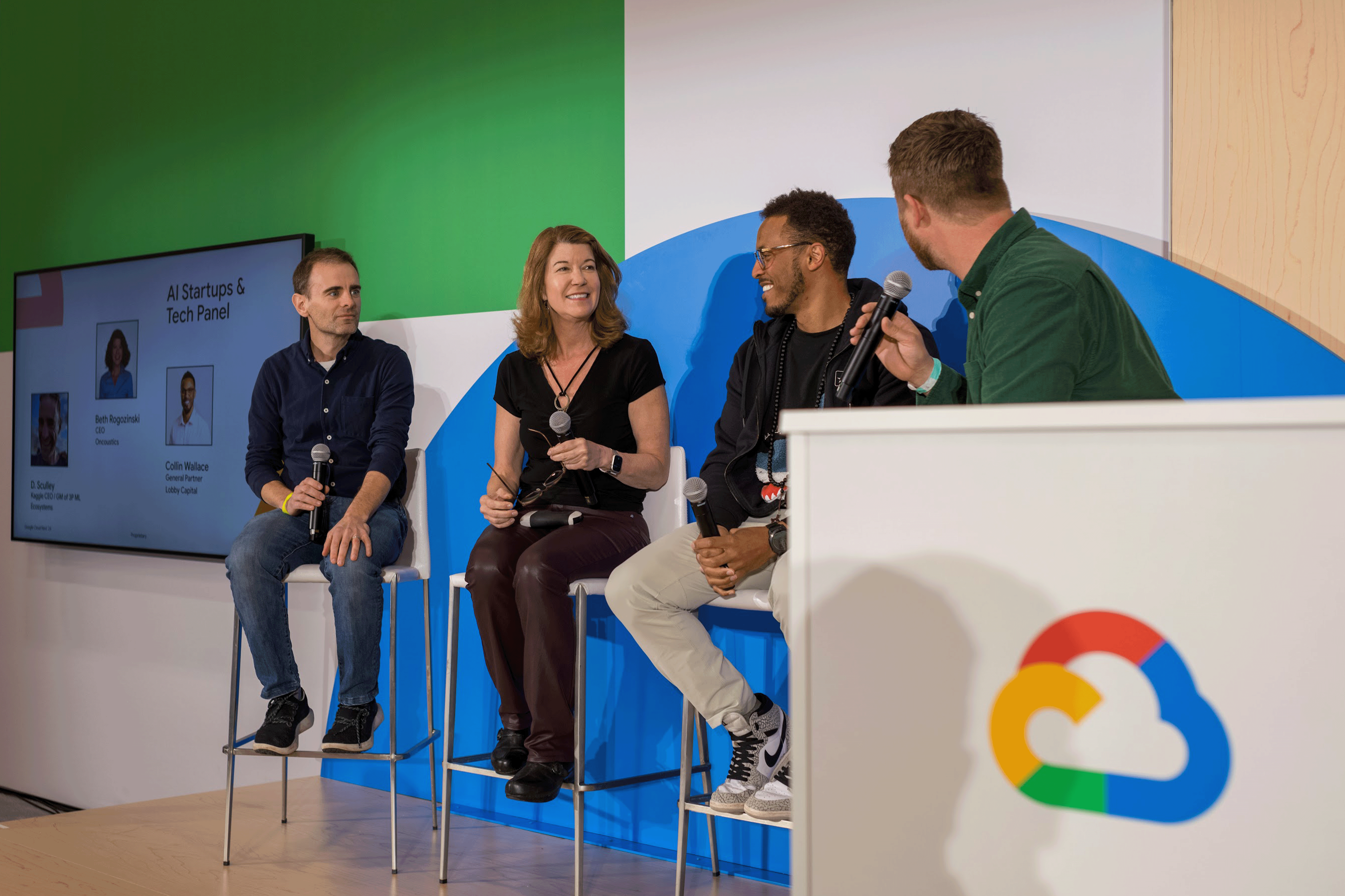 A panel of hosts is seated on a stage, engaged in a discussion.