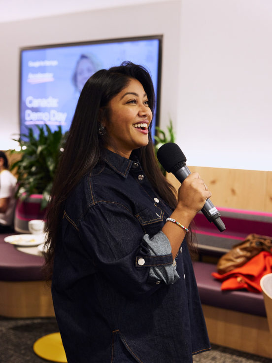 A young woman with a smile on her face speaks into a microphone while wearing a black shirt.