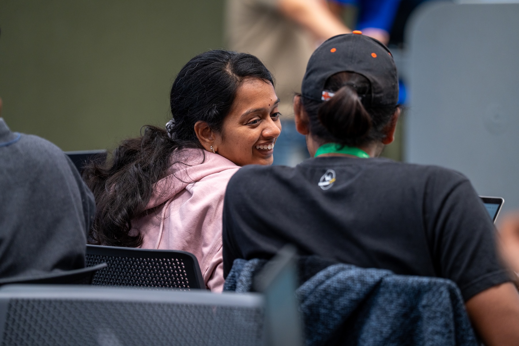 A woman who wore pink hoodie lookin to the person on her right and smiling.