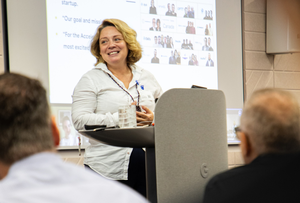 A gray-haired woman confidently presenting with a warm smile.