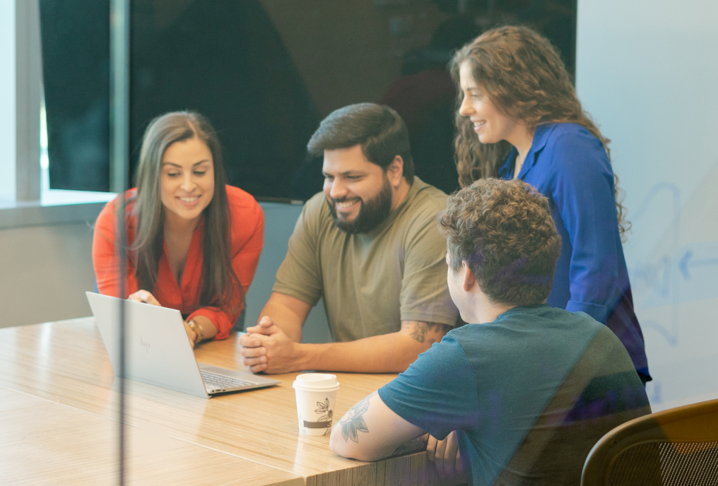 2 men and 2 women smiling while looking at laptop