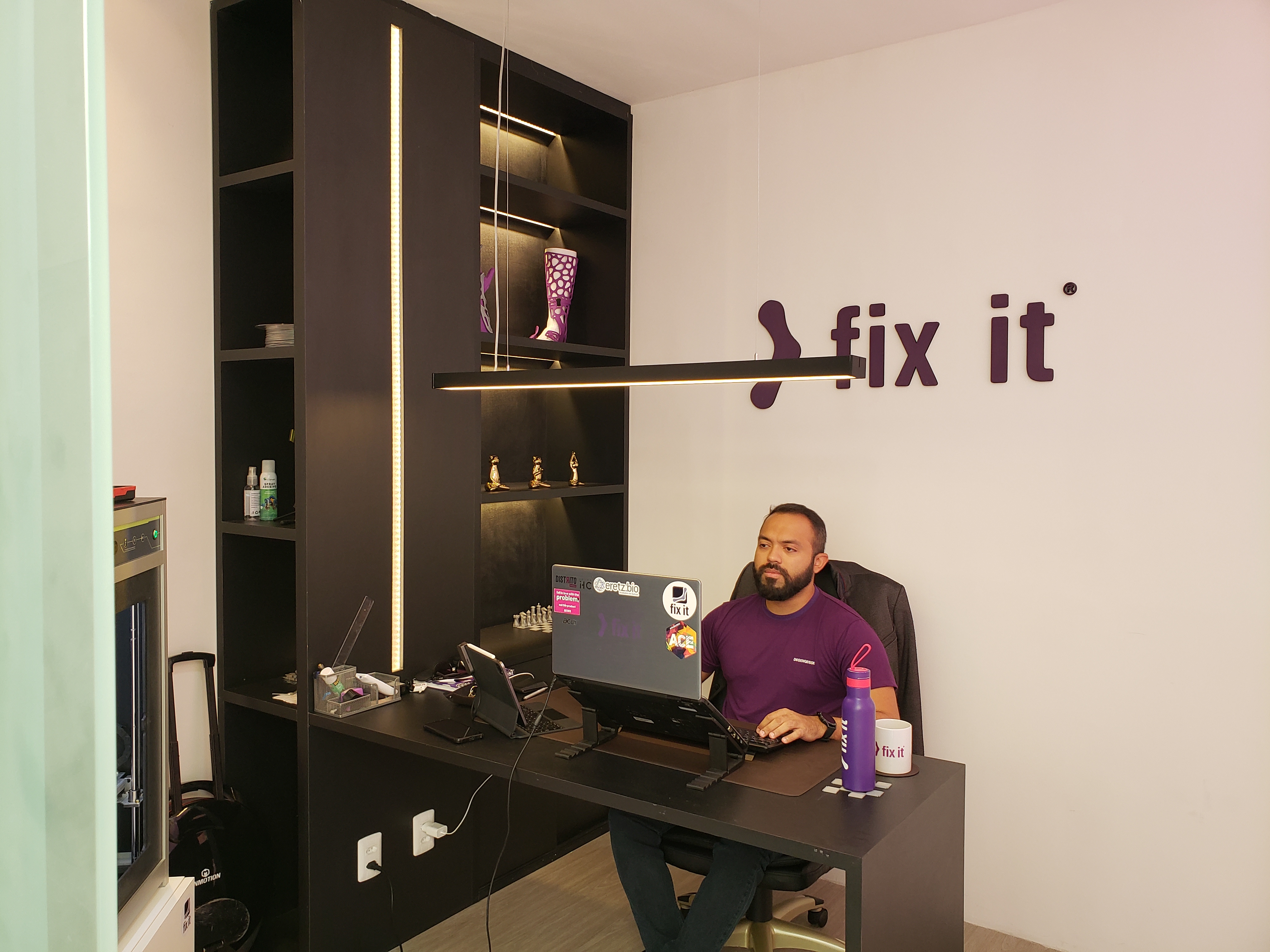 FixIt cofounder Hebert Costa works in the FixIt office. Across from him is a 3D printer and above his desk are FixIt prosthetics.