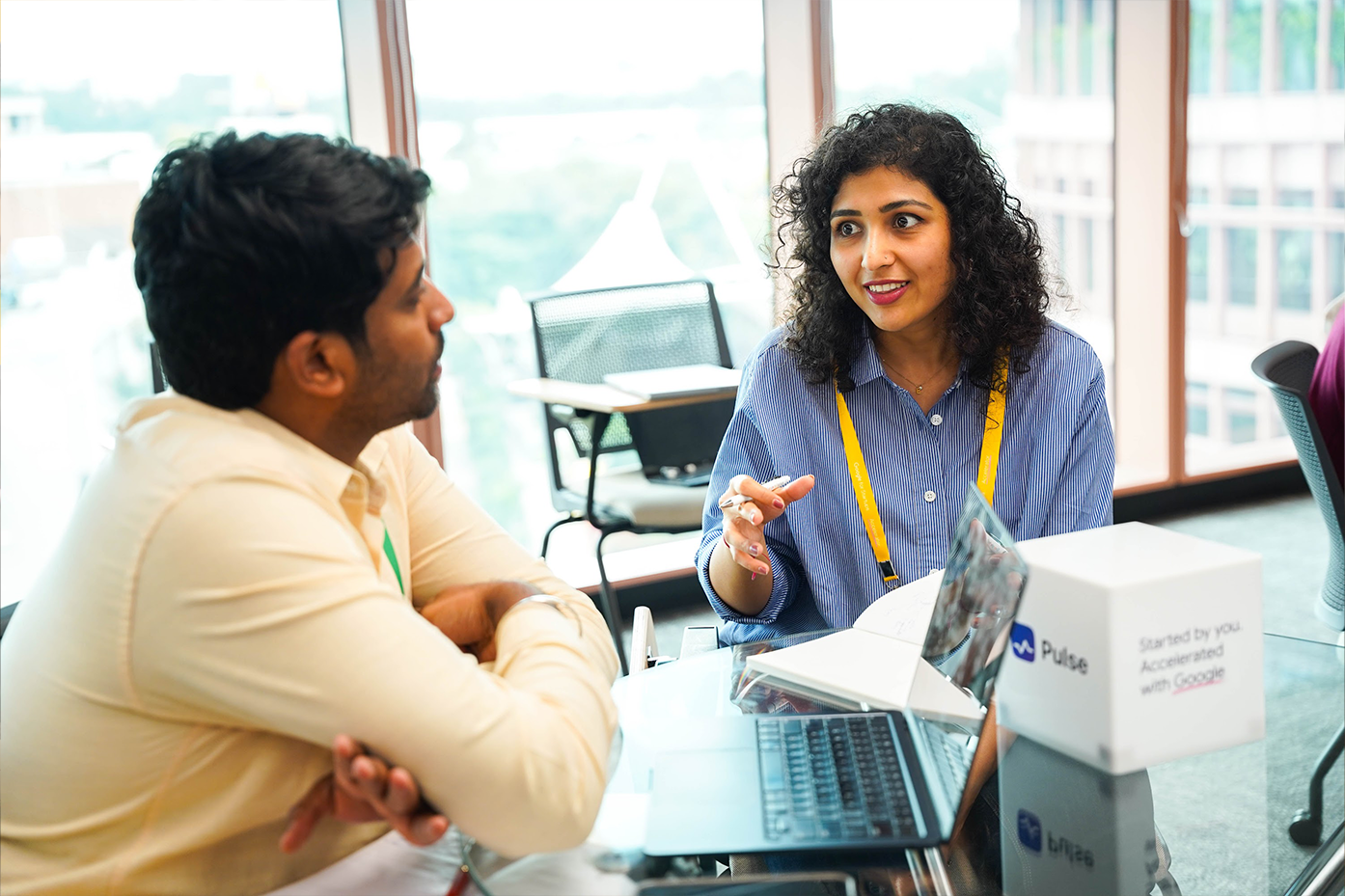 A woman and a man engaging in conversation while looking at a laptop screen.