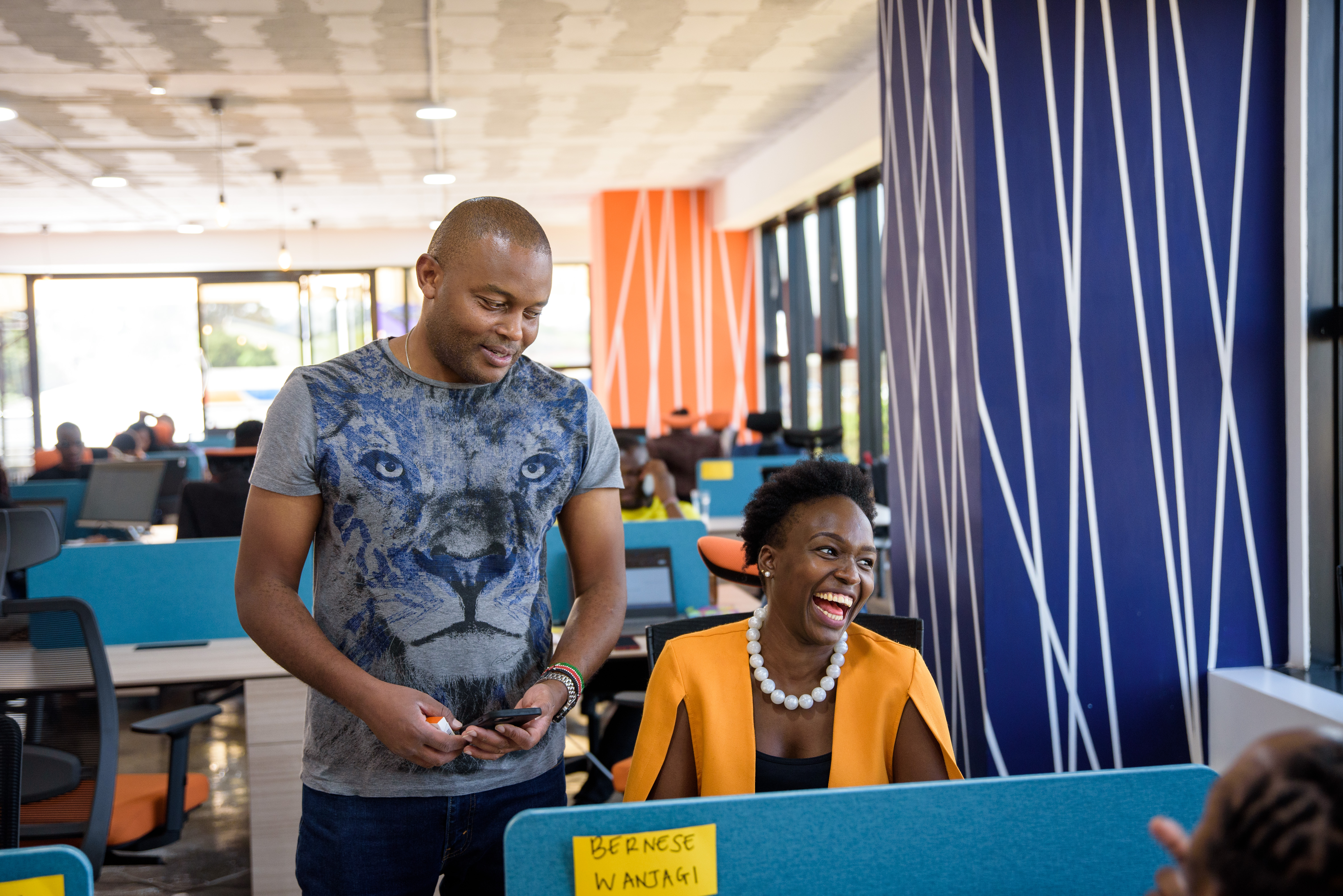 Photo of Mark, the founder of Amitruck, a Black man wearing a blue shirt with a lion on it. Mark is standing next to an employee of Amitruck, a Black woman with a yellow blazer who is smiling.