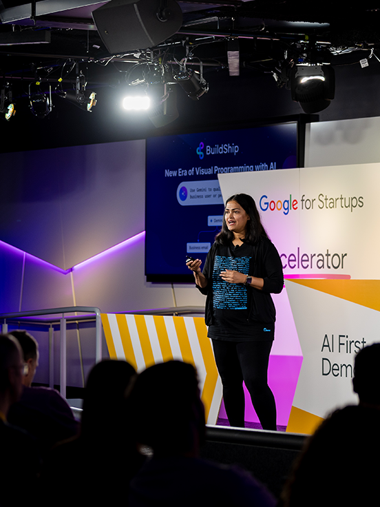 A lady on the event stage is addressing the audience while holding microphones.