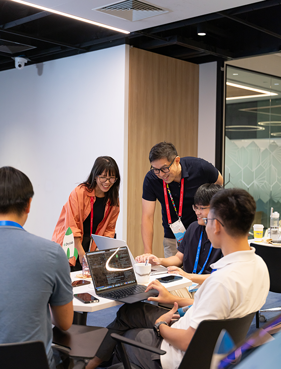 A conference room meeting where two people stand behind the host to view his laptop.