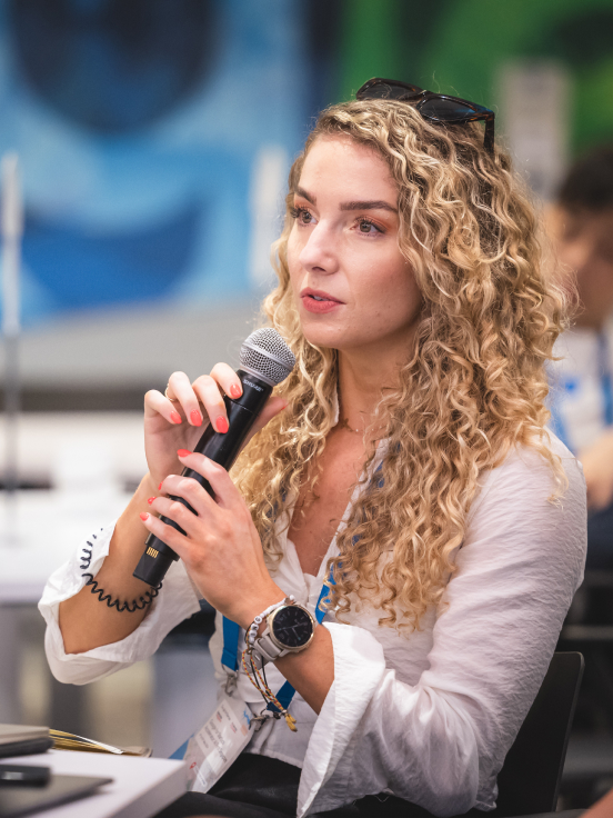 A woman with curly hair is speaking something on mic