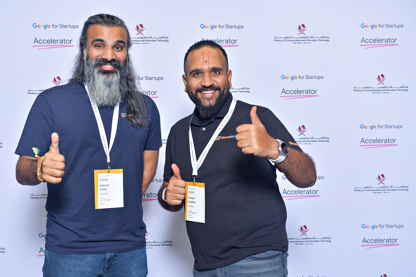 Two people wearing ID badges are posing for a photo in front of the event banner.