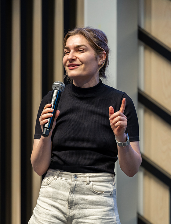 A lady is addressing a large event audience with a mic.