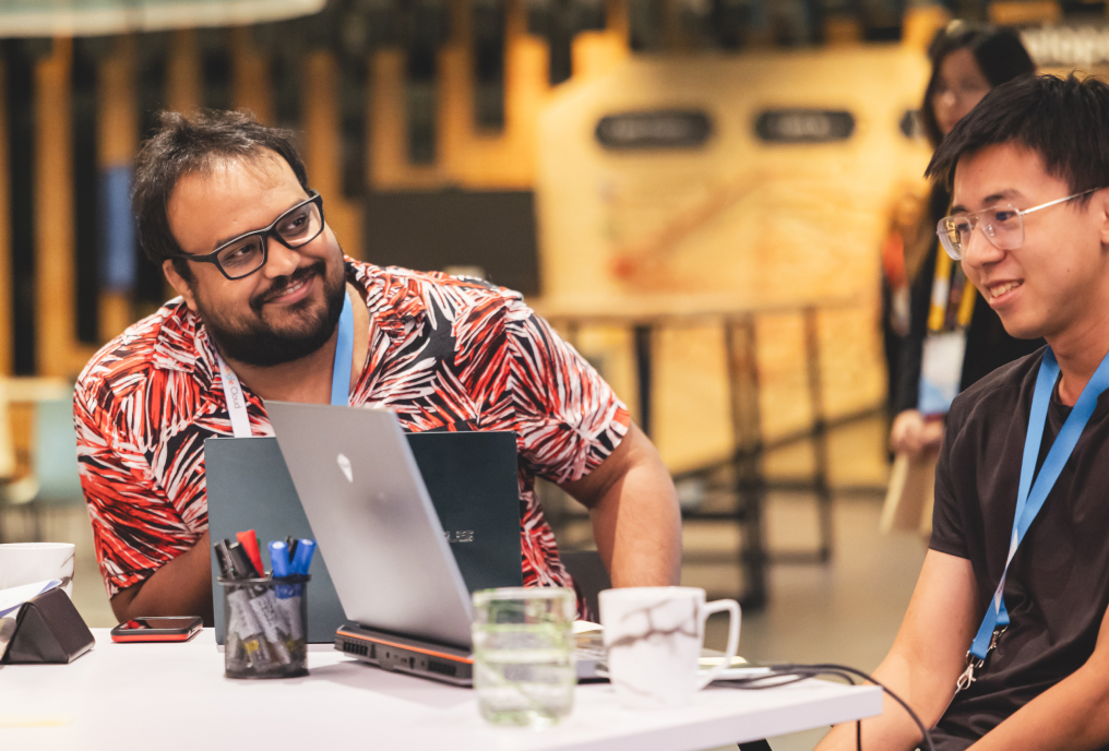 2 men talking while working on laptop