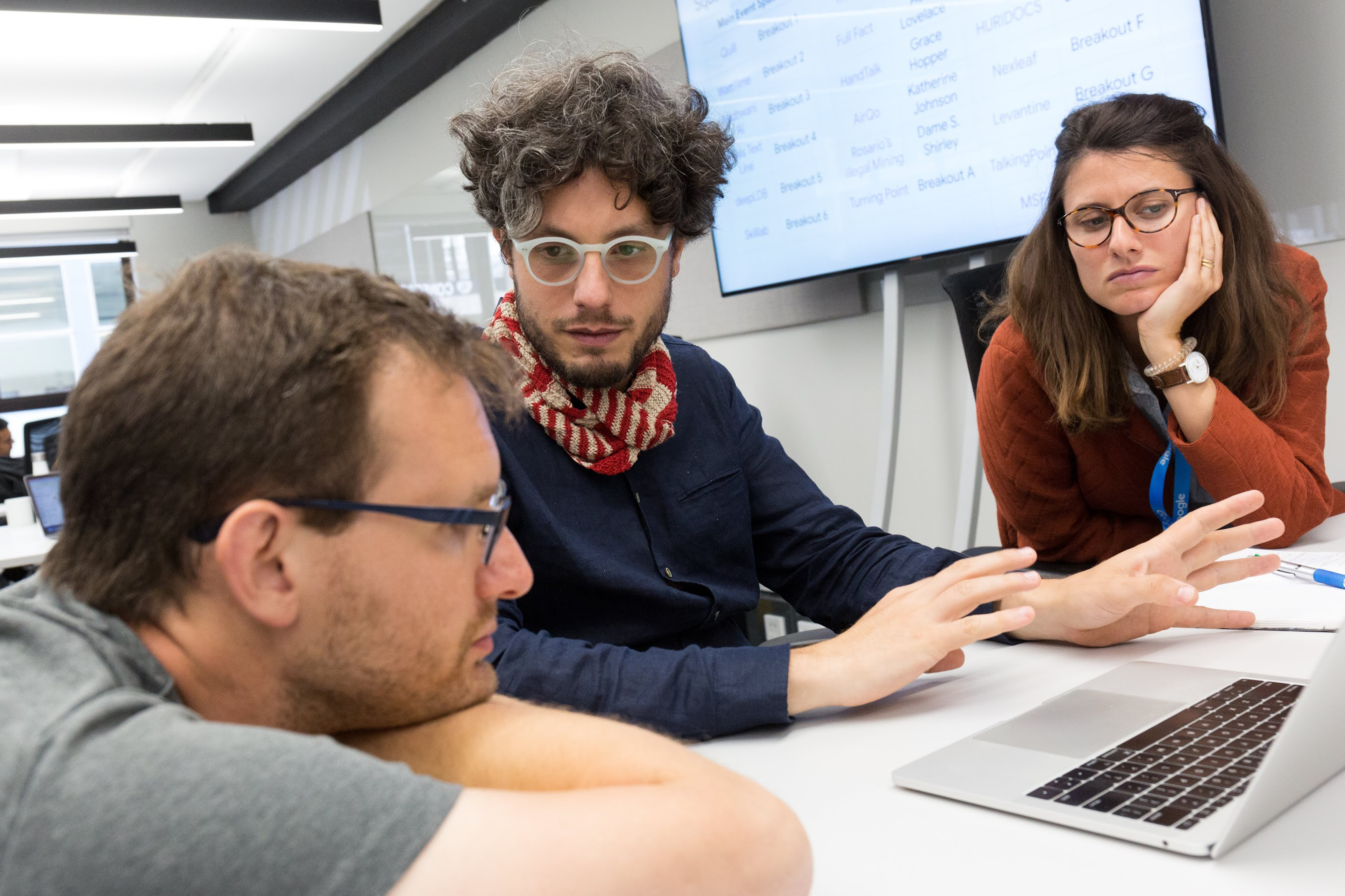 Three individuals are discussing something with a laptop on the table.
