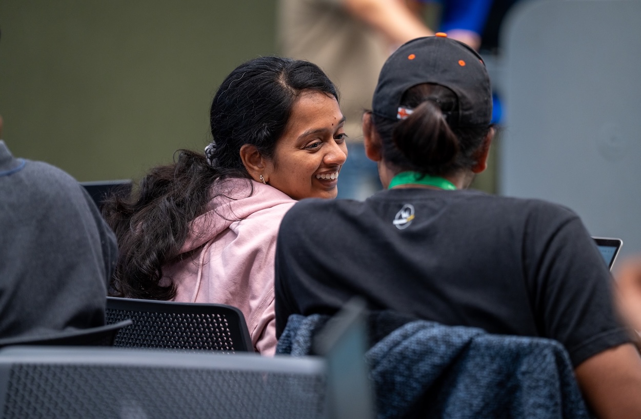 A woman who wore pink hoodie lookin to the person on her right and smiling.