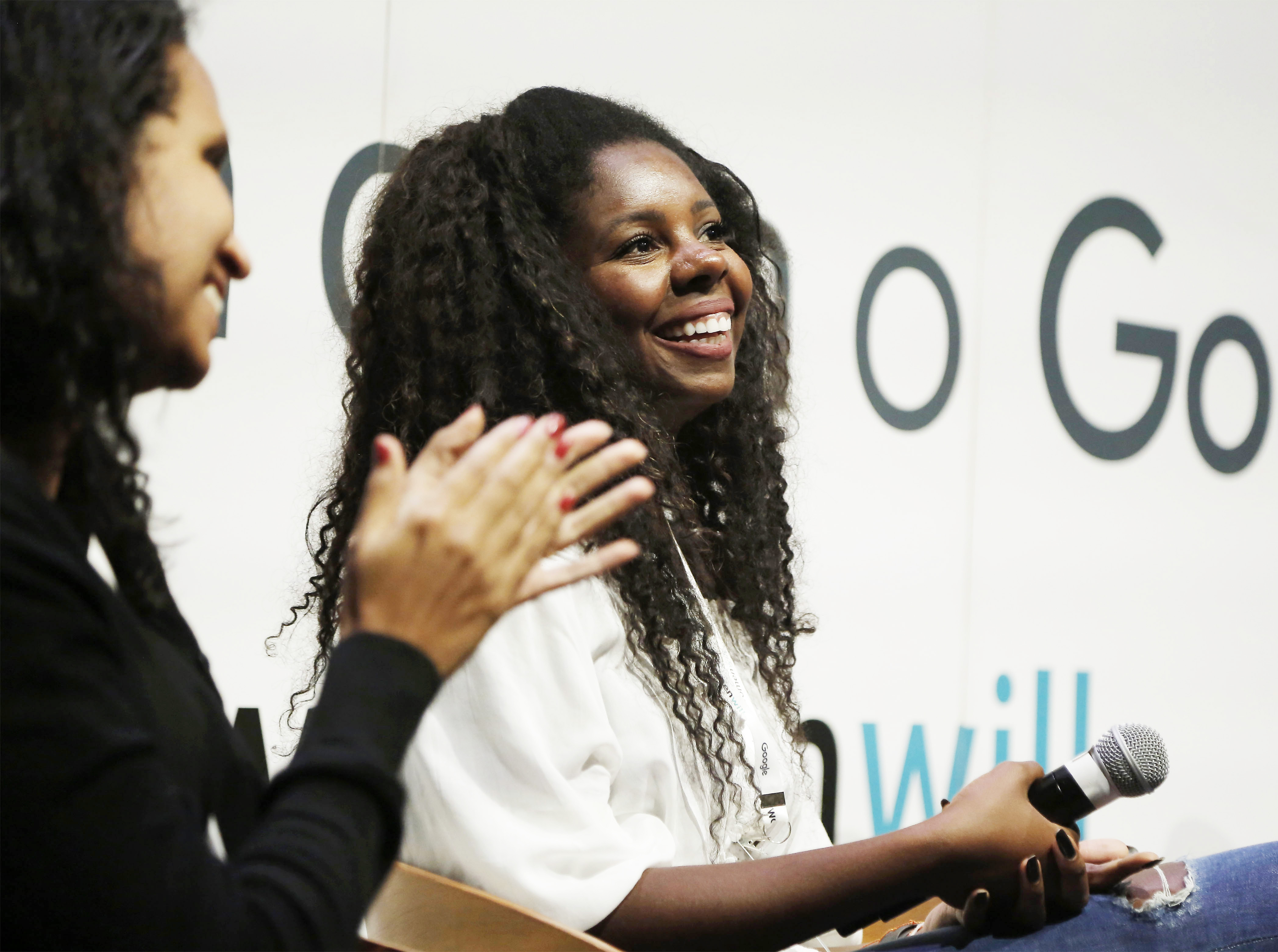 A woman wearing blue top in focus talking to another woman facing away from the camera.