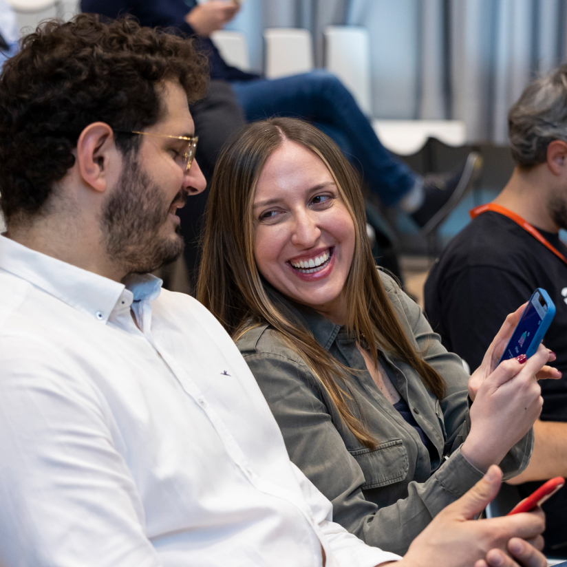 A seated woman is showing something on the phone to a man beside her