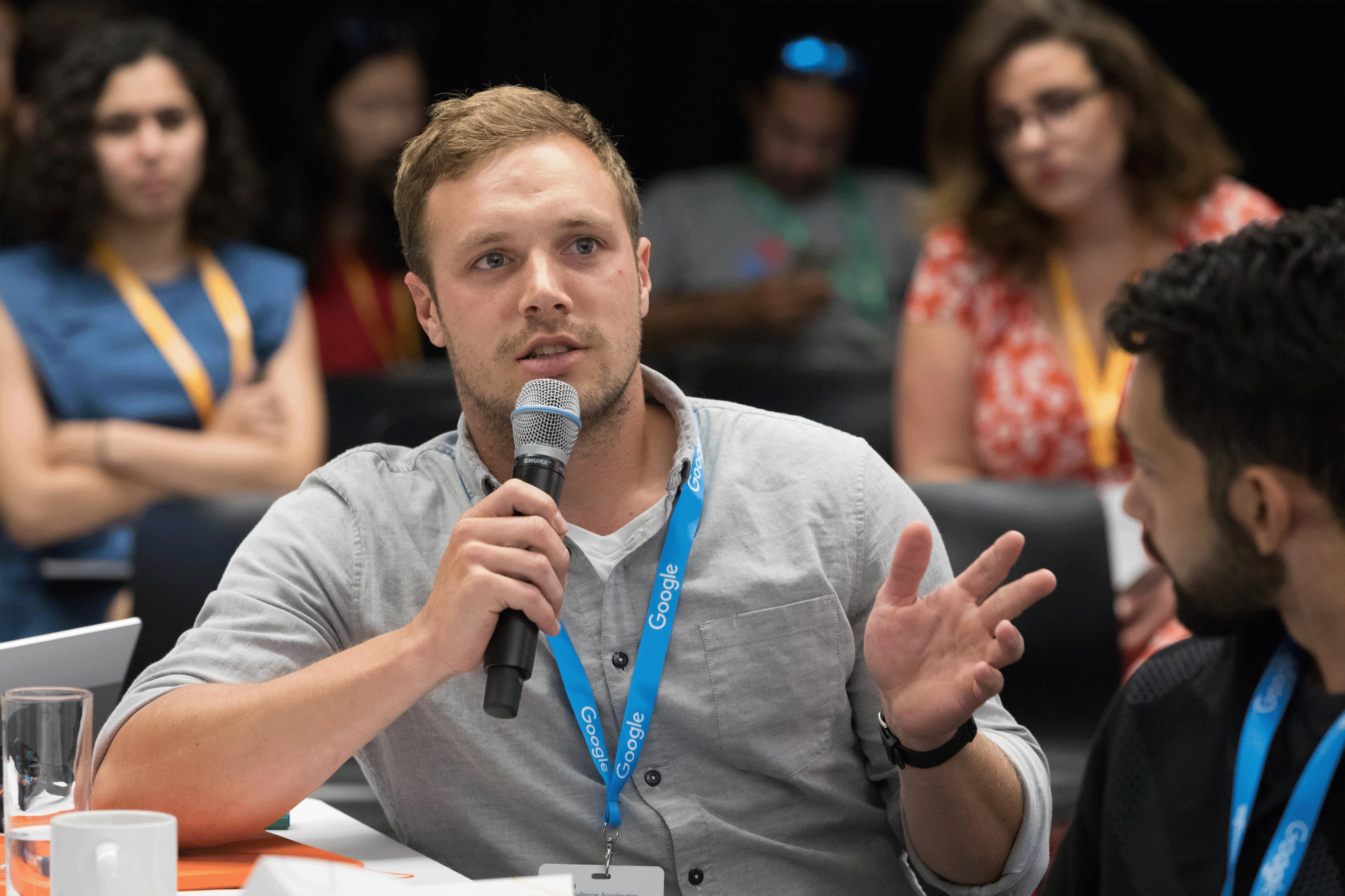 Seated at a table, a Google-tagged attendee is speaking to the host.