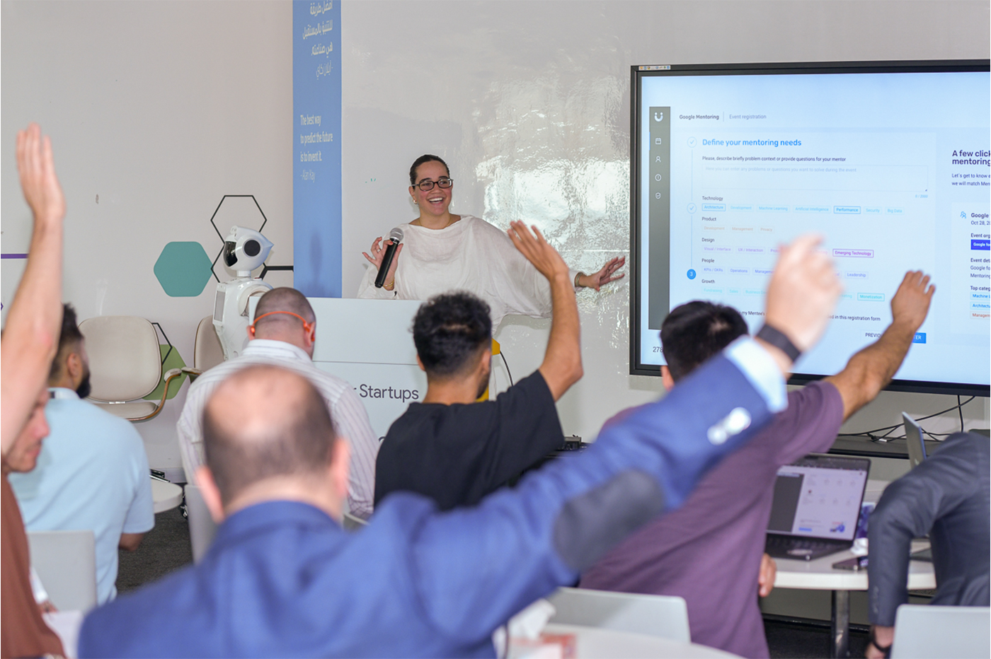 In a happy setting, the host is presenting, and attendees are raising their hands, ready to answer.